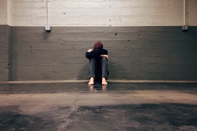 Junge unter Stress kauert sich vor einer Wand zusammen weil er kein Stressmanagement anwenden kann