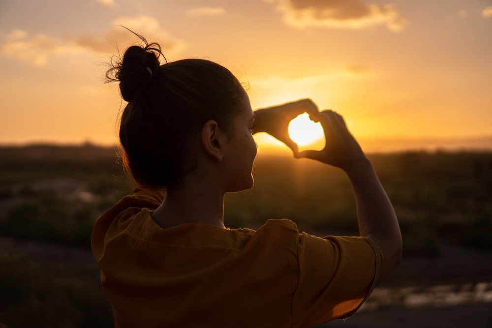 Selbstliebe: Mädchen formt ein Herz mit den Händen vor dem Sonnenuntergang